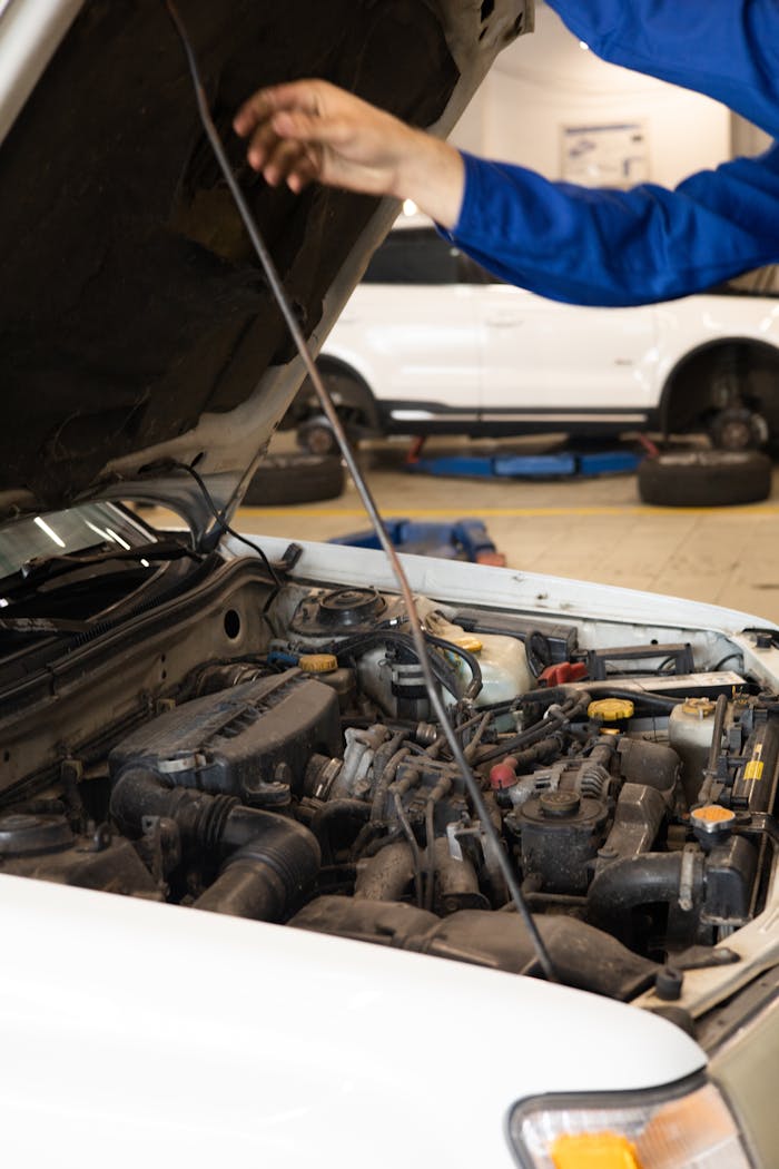 Close-up of mechanic inspecting car engine under open hood in an auto repair shop.